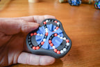 Hand holding a black triangular mechanical puzzle with blue, red, and white beads for brainteaser and fidget use. - andEleven - The Delta (3-Color)