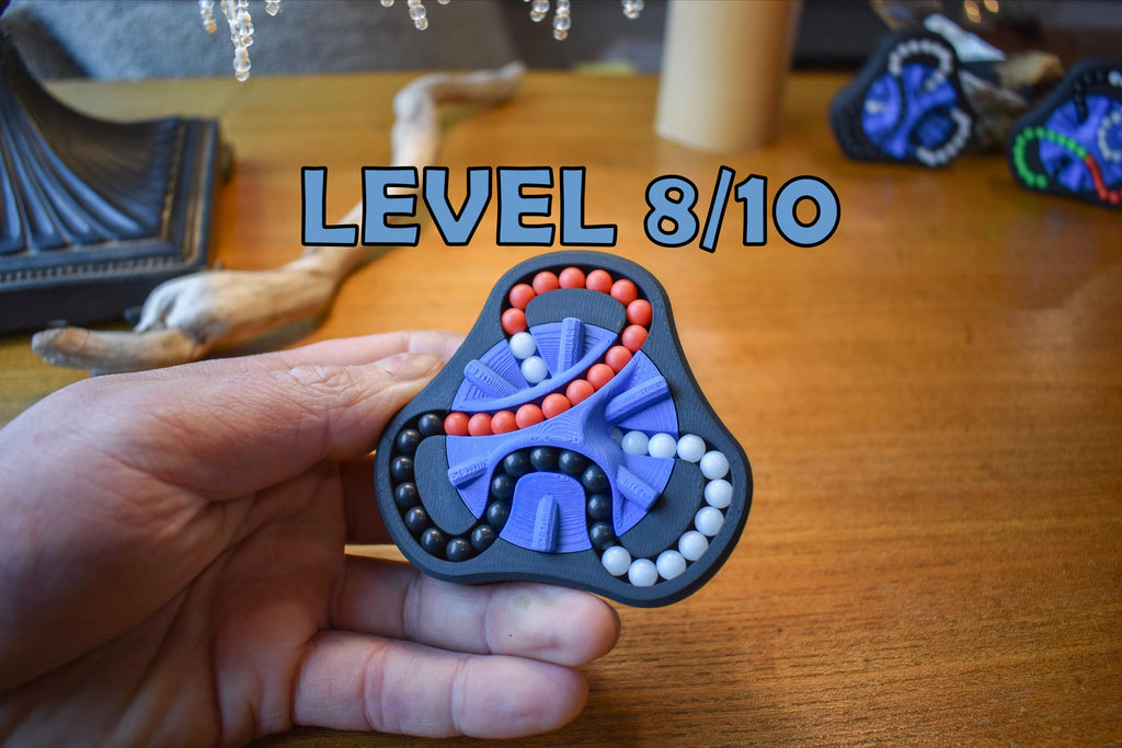 Hand holding The Delta 3-Color mechanical puzzle brainteaser fidget with red, blue, and white sliding beads at level 8 of 10. - andEleven - The Delta (3-Color)