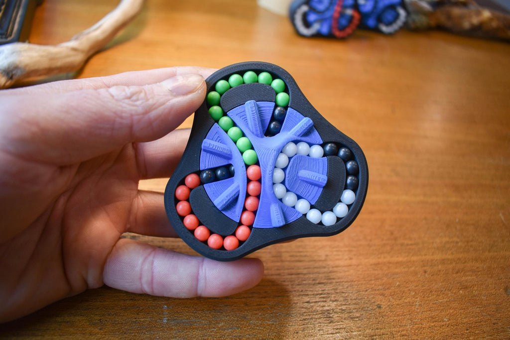 Compact Delta mechanical puzzle with red, green, blue, and black beads, ideal as a brainteaser fidget toy. - andEleven - The Delta (4-Color)