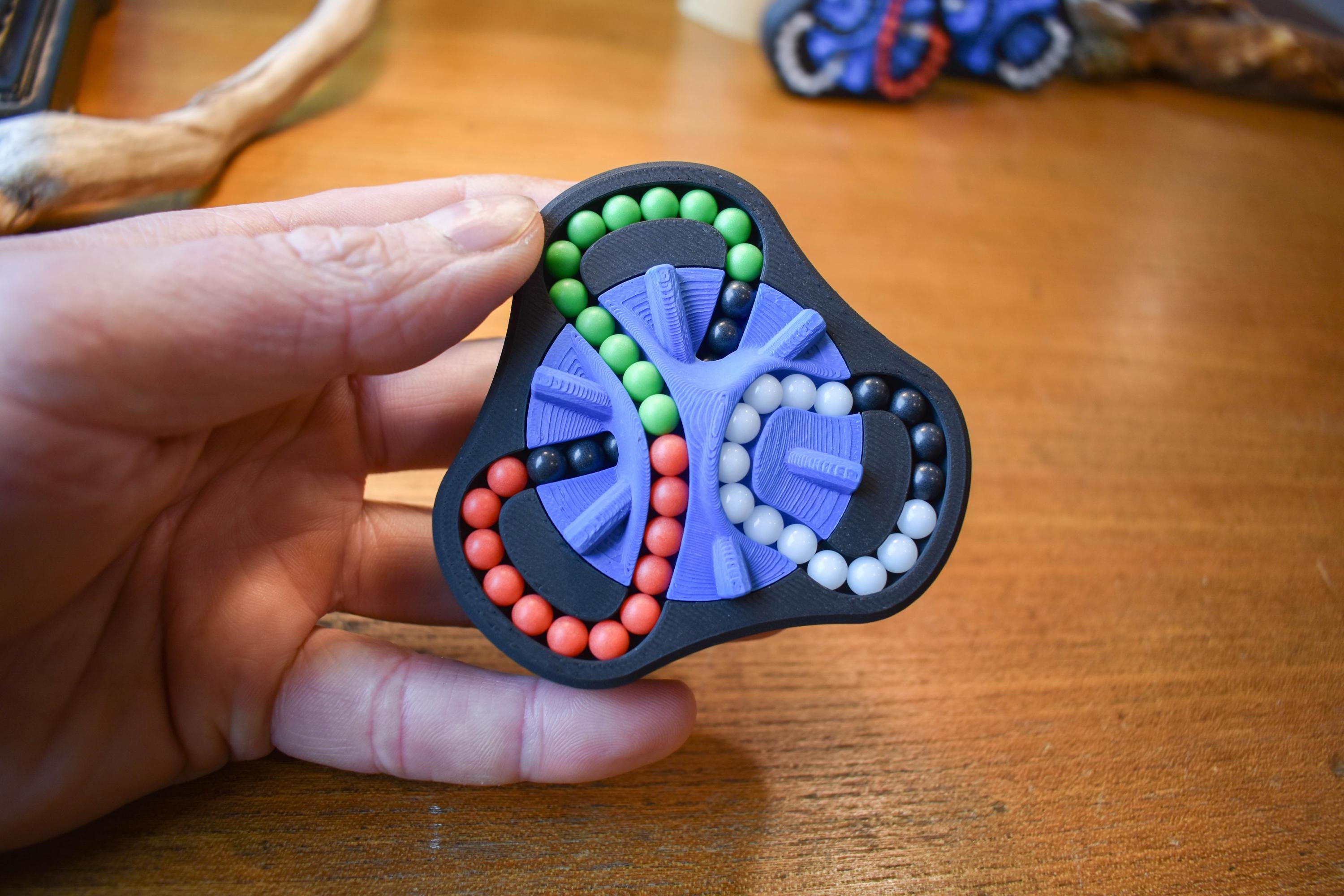 Compact Delta mechanical puzzle with red, green, blue, and black beads, ideal as a brainteaser fidget toy. - andEleven - The Delta (4-Color)