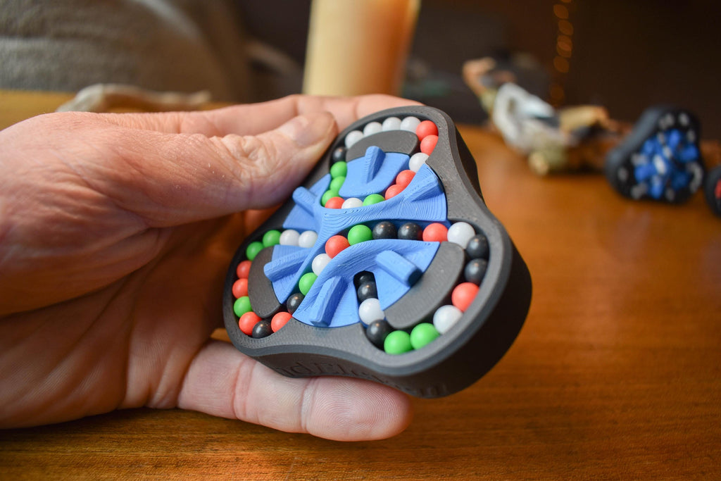 Hand holding black triangular mechanical puzzle with blue, red, green, and white beads, brainteaser fidget toy. - andEleven - The Delta (4-Color)