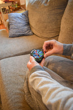 Hands manipulating a colorful four-color mechanical puzzle brainteaser fidget on a couch. - andEleven - The Delta (4-Color)