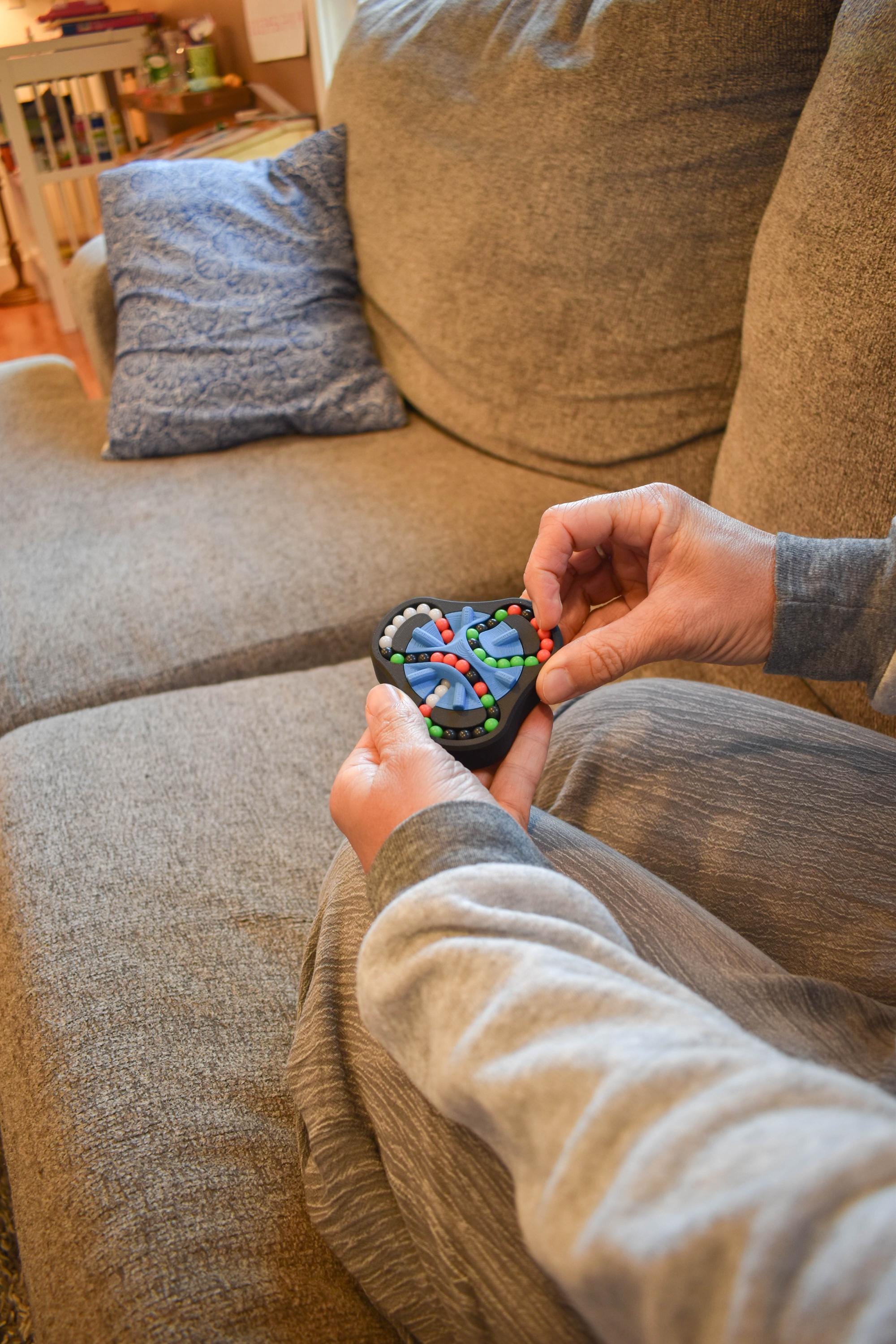 Hands manipulating a colorful four-color mechanical puzzle brainteaser fidget on a couch. - andEleven - The Delta (4-Color)